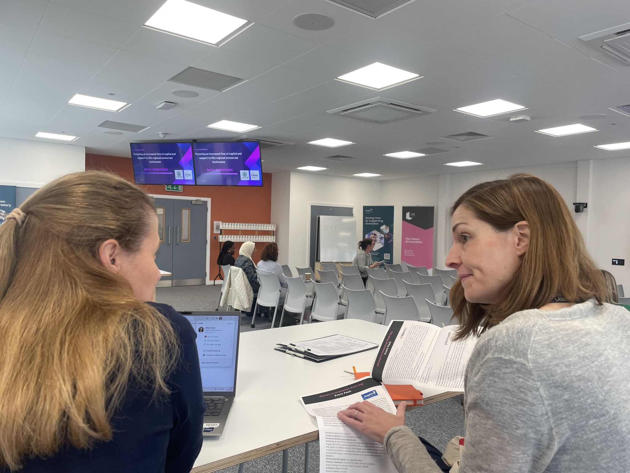 Two senior female members of the iiCON team discussing a pitch event